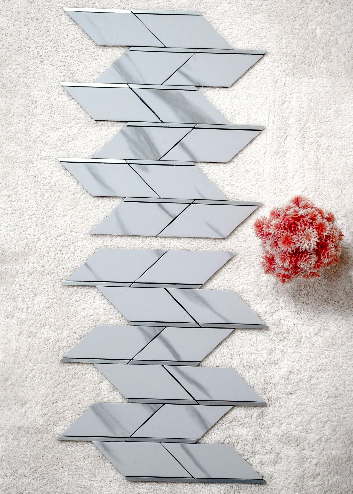 Geometric mirror tiles arranged in a pattern on a textured surface with a red flower.