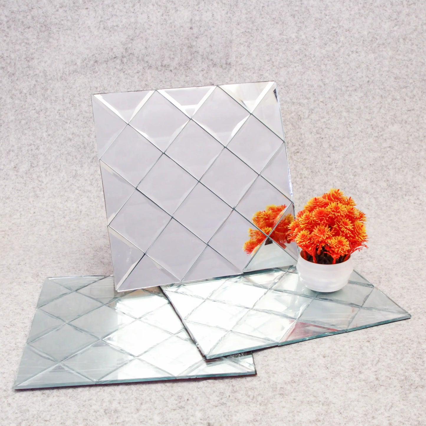 Three diamond-shaped mirror tiles on a light gray surface with a small potted plant.
