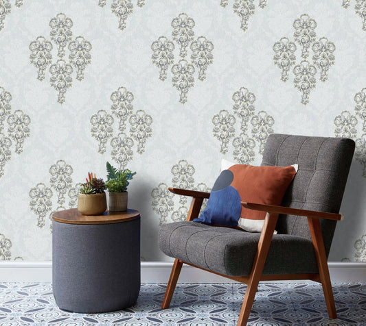 Gray armchair with colorful cushions next to a small round table with plants against a decorative wallpaper.