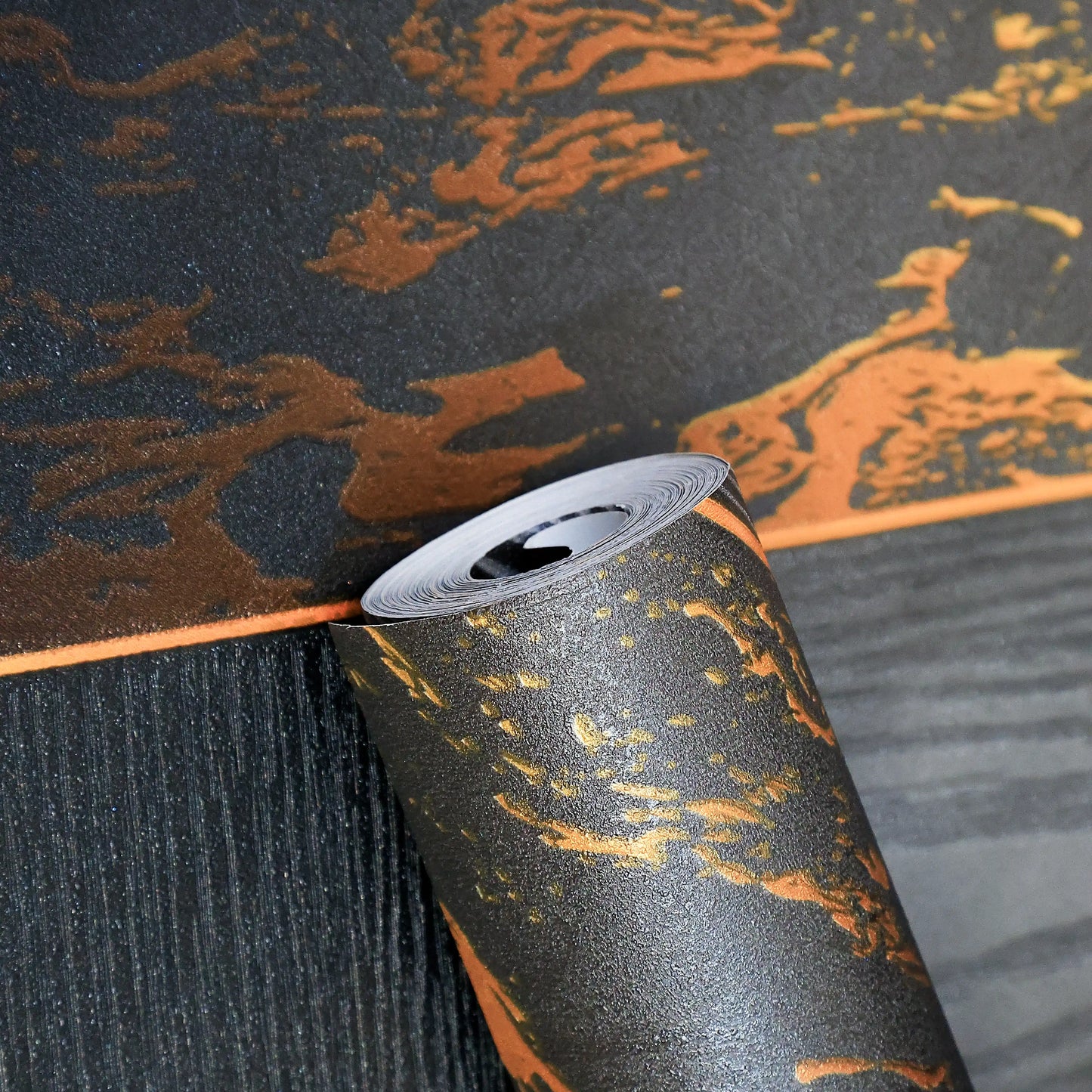 Roll of decorative wallpaper with black, orange, and gray pattern on a textured surface.