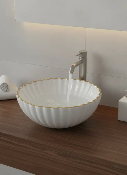 White ceramic sink with gold rim on a wooden countertop in a bathroom setting.