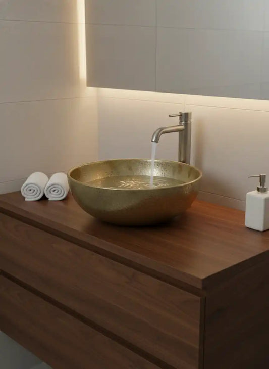 Gold sink on a wooden vanity with a faucet and soap dispenser.