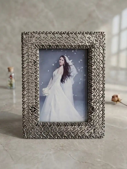 Decorative photo frame with a woman in a white dress inside, on a light surface.