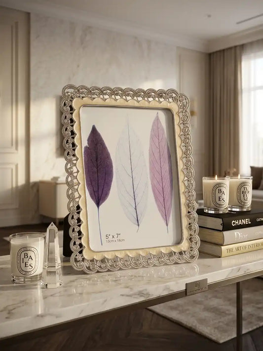Decorative frame with pressed leaves on a marble surface with candles and books.