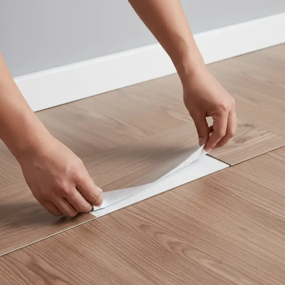Person applying a strip of tape to a wooden floor