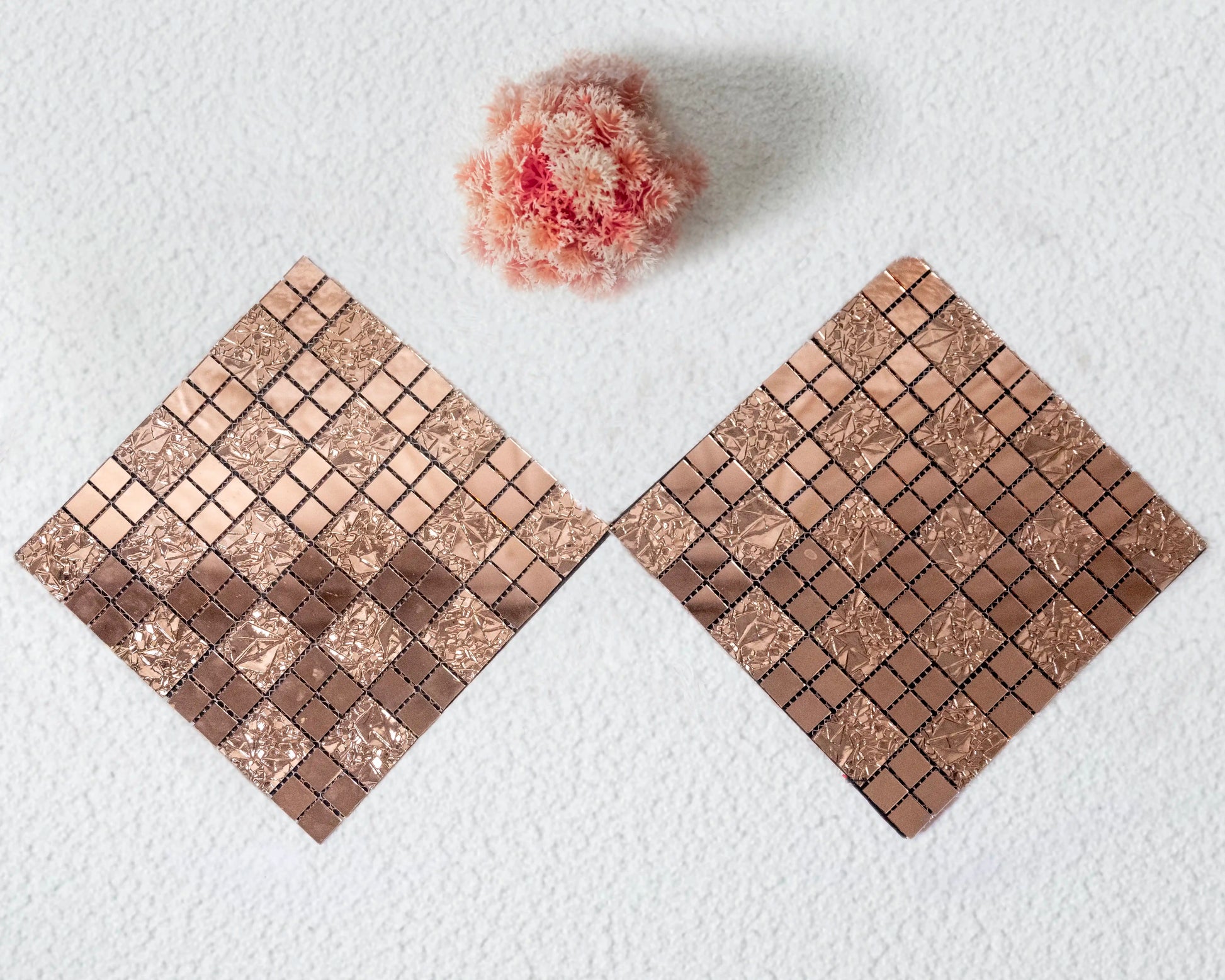 Two square coasters with a mosaic tile design on a white surface with a pink flower.