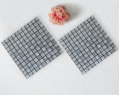 Two gray textured square mats on a white surface with a pink flower.