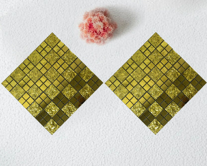 Two gold mosaic square coasters on a white surface with a pink flower.