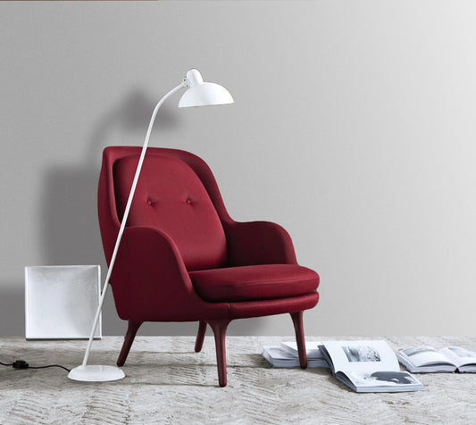 Red armchair with a white floor lamp on a wooden floor against a gray wall.