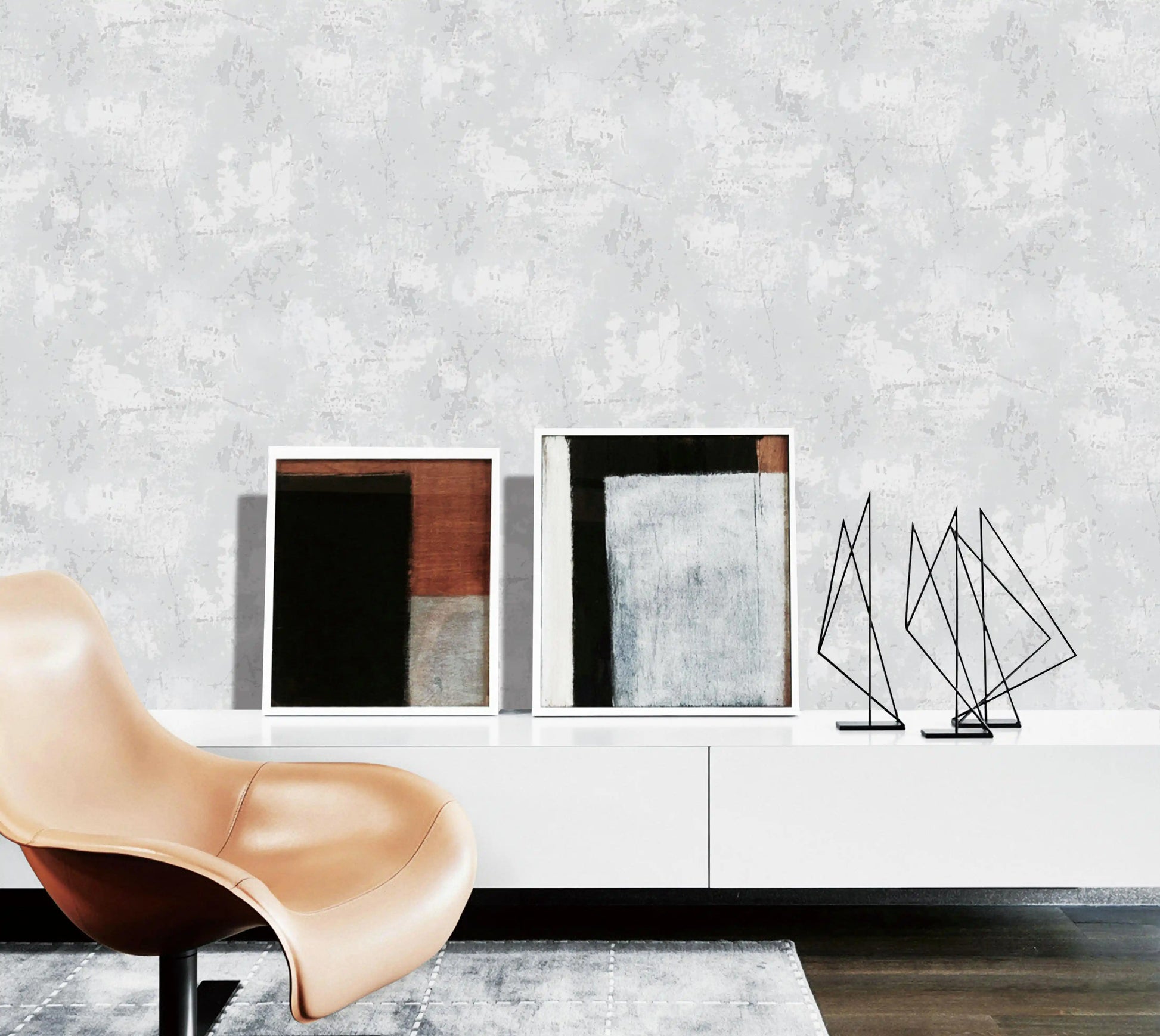 Modern interior with a beige chair, abstract sculptures, and framed art on a white shelf against a textured gray wall.