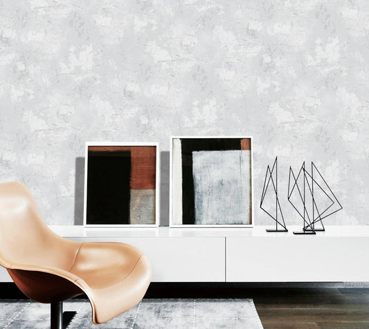 Modern interior with a beige chair, abstract sculptures, and framed art on a white shelf against a textured gray wall.