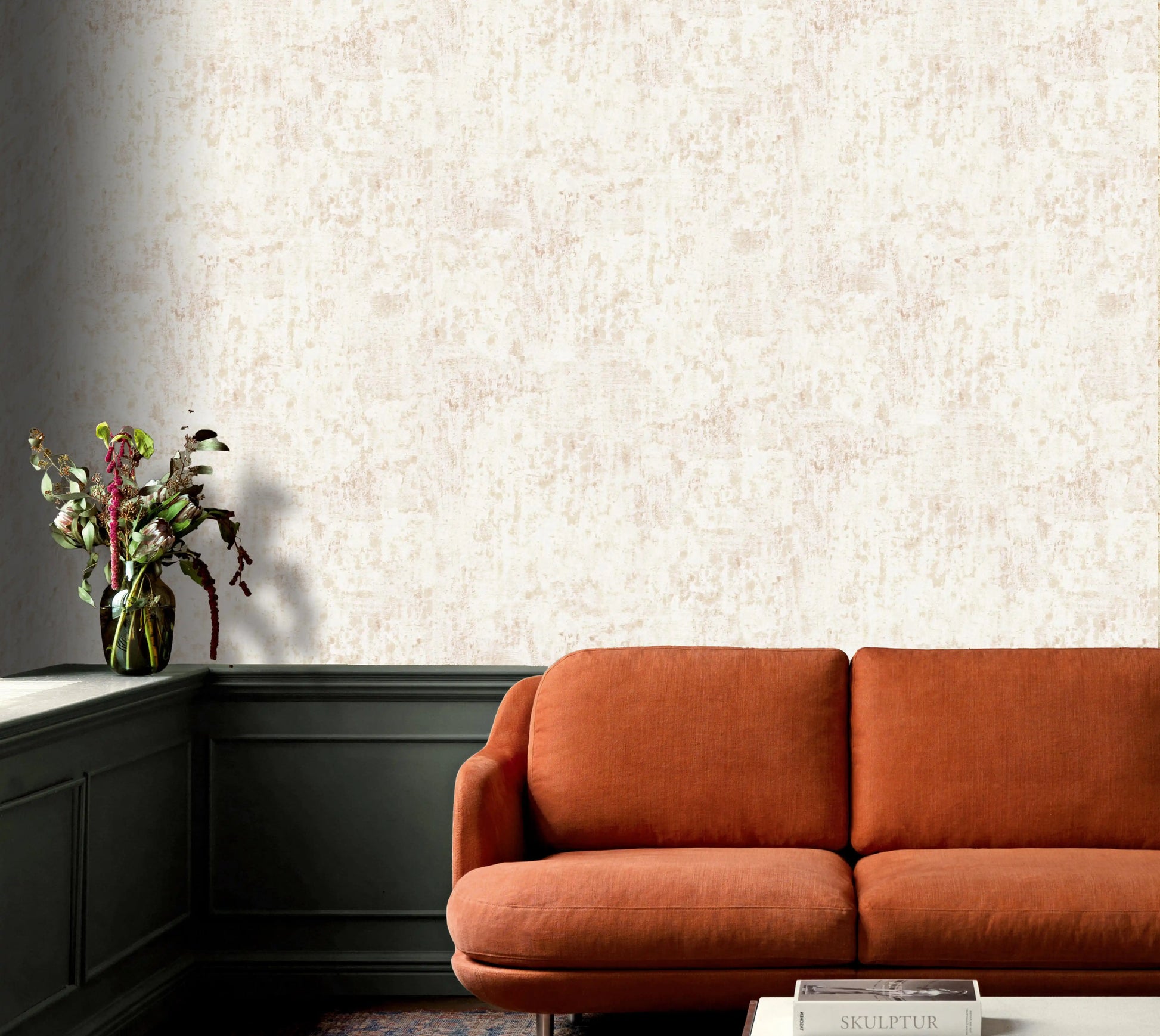 Orange sofa against a textured wall with a vase of flowers on a shelf.