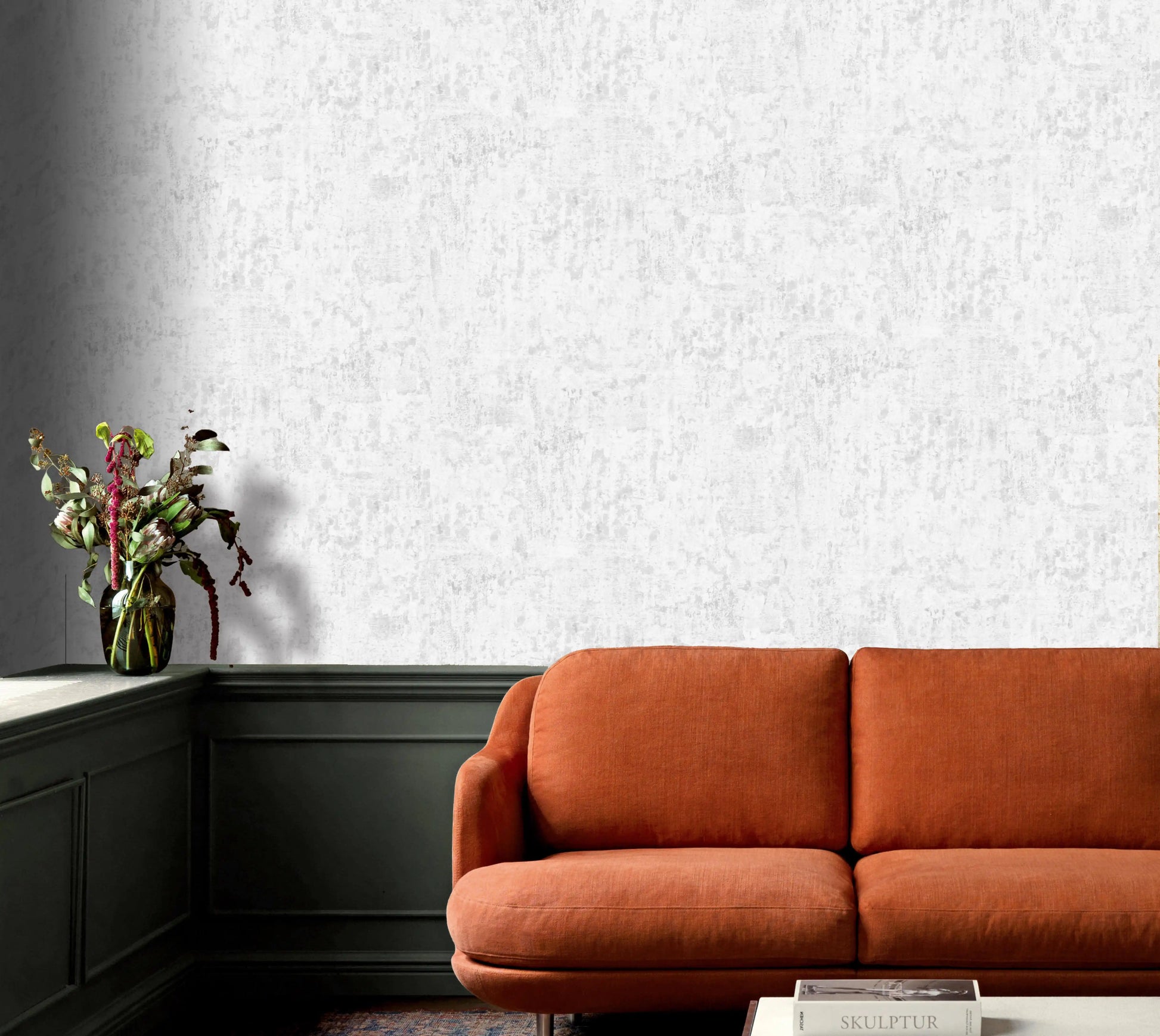 Orange sofa in a room with textured white wallpaper and a vase of flowers on a shelf.