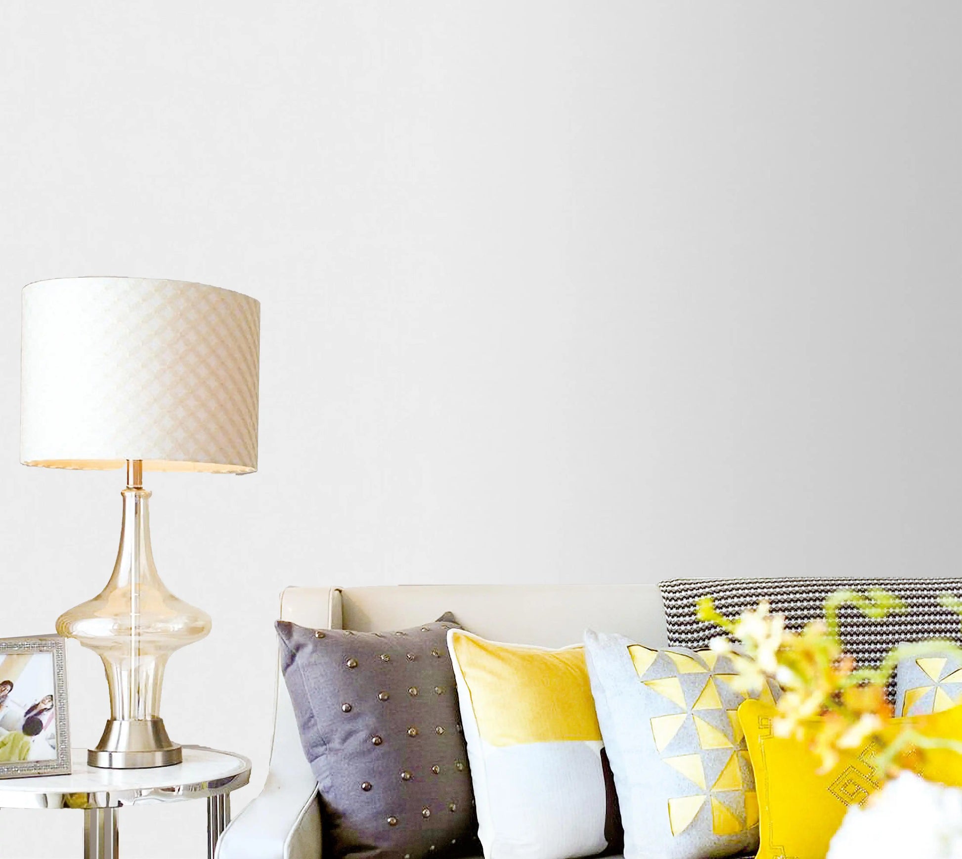 Living room with a couch featuring colorful pillows, a lamp, and a vase with flowers on a white background.