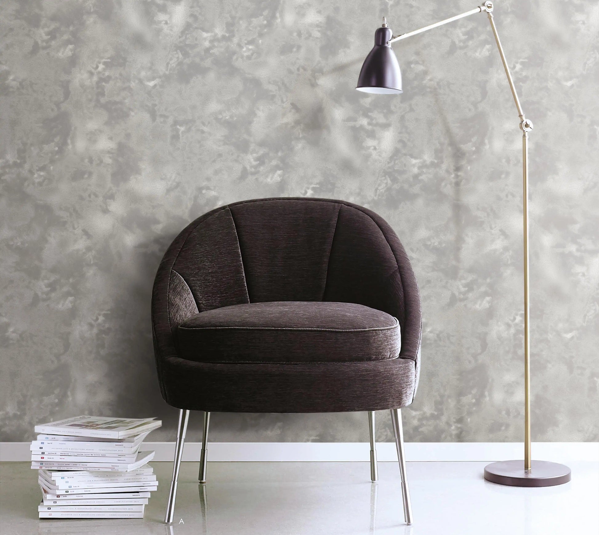 Brown armchair with a stack of books against a gray textured wall.